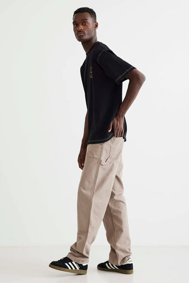T-shirt noir de WOODBIRD, à manches courtes et avec des coutures contrastantes, porté avec un pantalon kaki et des baskets noires.