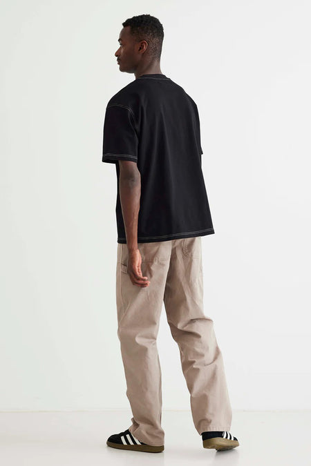 T-shirt noir de WOODBIRD, à manches courtes et avec des coutures contrastantes, porté avec un pantalon beige et des baskets noires.