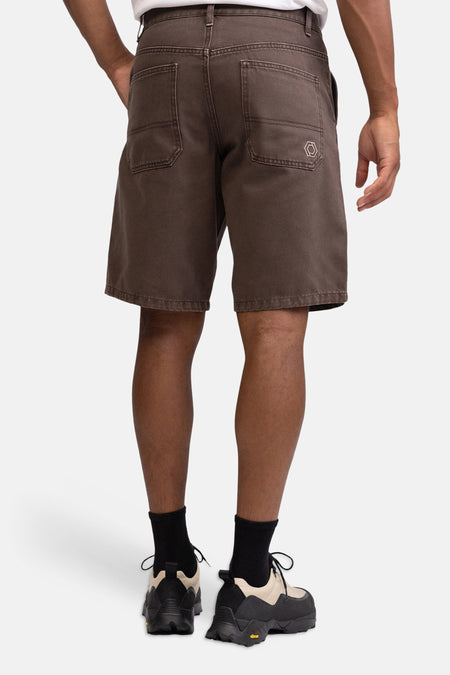 Bruine jeansshort met zakken en hexagon logo van REDEFINED REBEL, achterzijde weergegeven, model draagt wit shirt en zwarte sokken