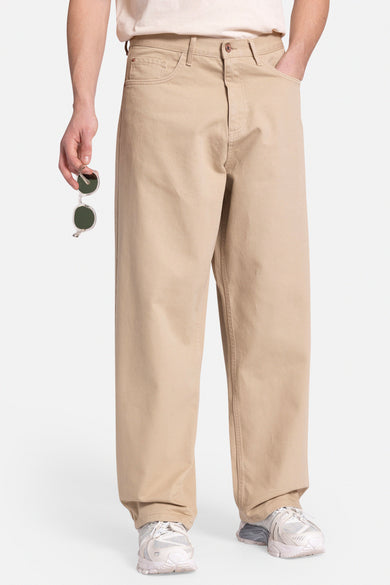 Pantalon beige de REDEFINED REBEL, avec un cactus brodé sur la poche arrière, associé à un T-shirt imprimé et des baskets blanches.