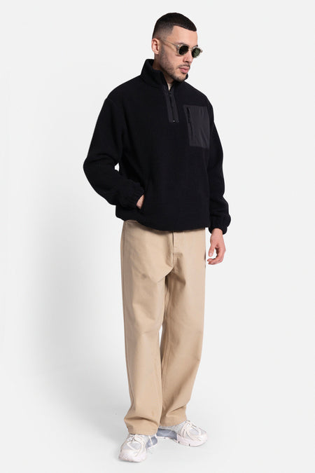 Pantalon beige de REDEFINED REBEL, avec des jambes larges et associé à une veste en fleece noire et à des baskets blanches.