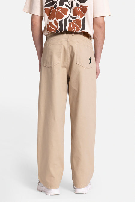 Beige broek van REDEFINED REBEL, met een geborduurde cactus op de achterzak, gecombineerd met een bedrukt T-shirt en witte sneakers.
