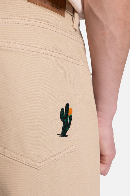 Pantalon beige de REDEFINED REBEL, avec un cactus brodé sur la poche arrière.
