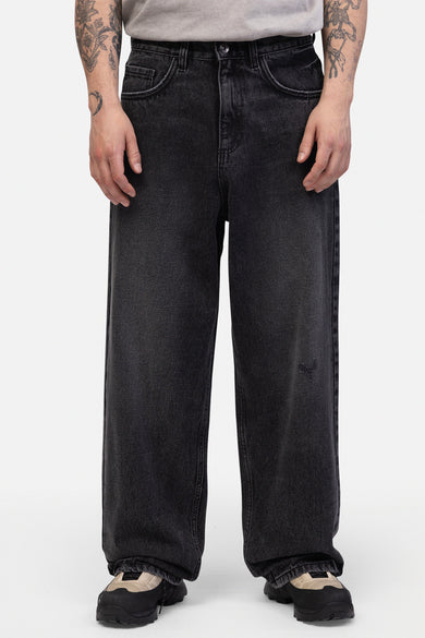 Jean délavé gris foncé de REDEFINED REBEL, avec une petite imperfection sur la jambe droite et des chaussures noires.