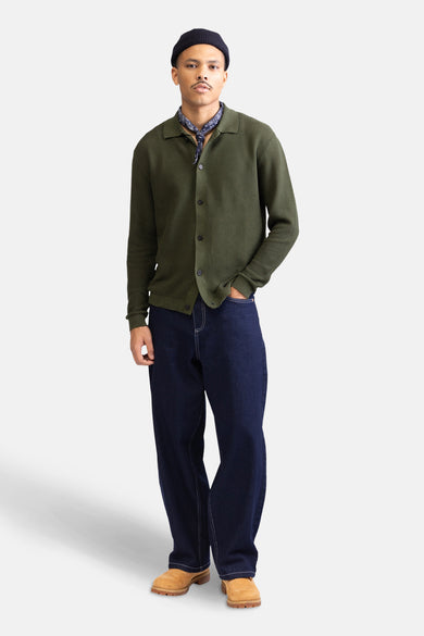Jean décontracté en denim bleu marine de REDEFINED REBEL, avec des surpiqures blanches, porté avec un cardigan vert et une bandana.