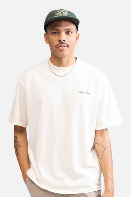 T-shirt écru à manches courtes de REDEFINED REBEL, avec modèle portant un chapeau vert et un pantalon beige.