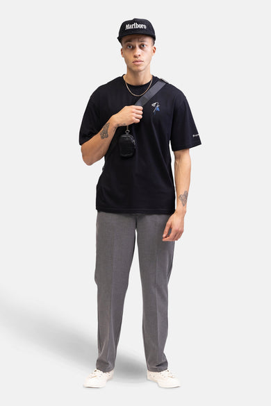 T-shirt noir à manches courtes de REDEFINED REBEL, avec un motif floral brodé et porté avec un casque et un pantalon gris.