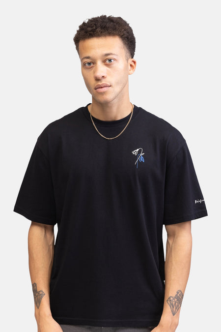 T-shirt noir à manches courtes de REDEFINED REBEL, avec un motif floral sur la poitrine et une signature sur la manche.