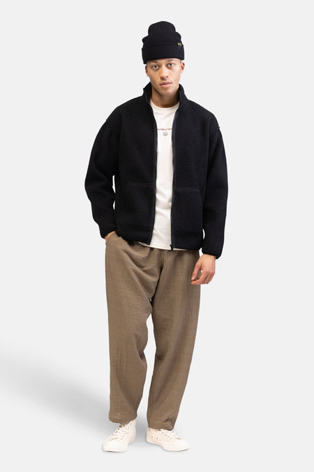 T-shirt écru à manches courtes de REDEFINED REBEL, porté sous une veste en fleece noire, avec un chapeau noir et des pantalons marron.
