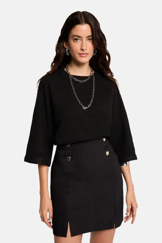 Jupe courte noire de Morgan De Toi, avec des boutons décoratifs et des fentes à la base, associée à une veste noire et des bijoux argentés.