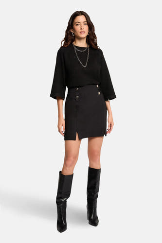 Zwarte korte rok van Morgan De Toi, met een split en gouden knopen. Gedragen met een zwarte top, zilveren ketting en zwarte laarzen.
