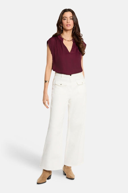 Chemisier bordeaux sans manches de Morgan De Toi, avec un col en V et combiné avec un pantalon blanc et des bottines marron.