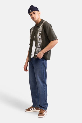 Chemise tricotée verte à manches courtes de REDEFINED REBEL, avec motif géométrique blanc et marron. Portée sur un t-shirt blanc.