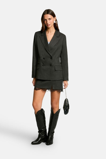 Jupe grise courte de Morgan De Toi, finie avec du galon, associée à un blazer et des bottes hautes.