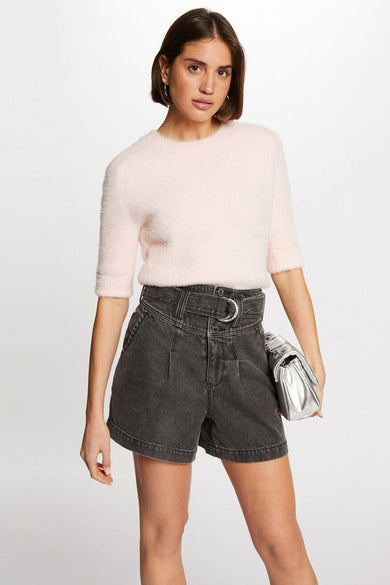 Vrouw met roze trui en grijze shorts, zilveren tas, witte achtergrond.
