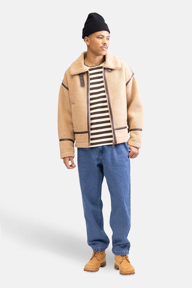 Pull marron de REDEFINED REBEL avec des rayures horizontales, associé à une veste beige, des jeans bleus et des bottes marrons.