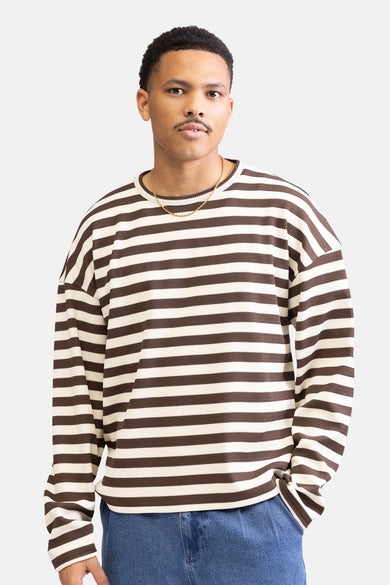 Pull-over marron de REDEFINED REBEL avec un motif rayé, porté avec une chaîne d'or et un pantalon de denim.