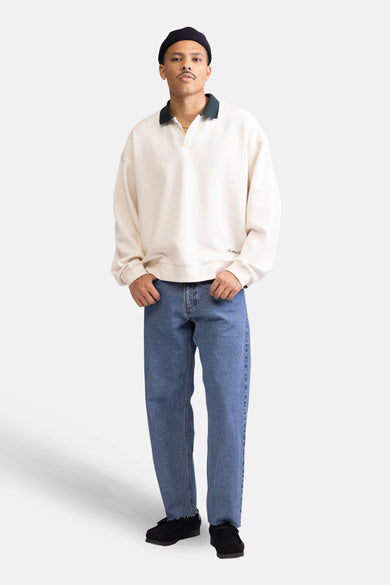 Gilet écru de REDEFINED REBEL, avec un col vert foncé et porté avec des jeans bleus et des chaussures noires.