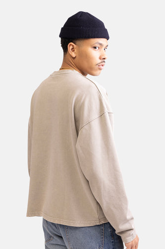 Man met muts, beige trui en jeans, over de schouder kijkend.