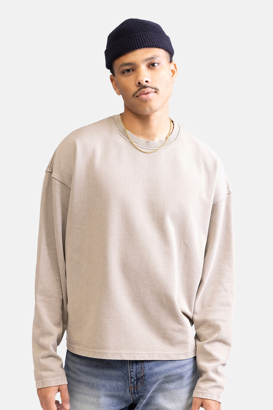 Man met muts, beige sweater en gouden ketting.