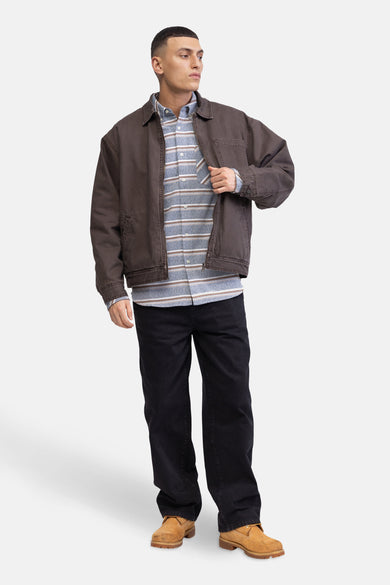 Man met bruine jas, gestreept shirt, zwarte broek en beige schoenen.