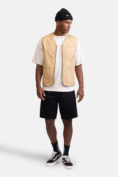 Manteau sans manches beige de REDEFINED REBEL, porté sur un t-shirt blanc, avec des short noirs et des baskets basses.
