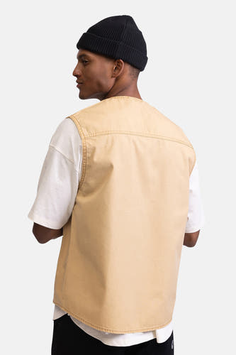 Beige mouwloze jas van REDEFINED REBEL, met stiksels op de schouder, gecombineerd met een wit T-shirt en zwarte beanie.
