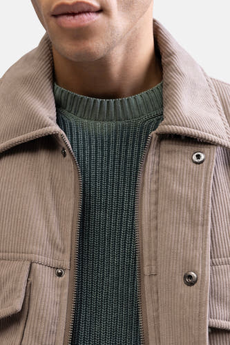 Manteau court beige de REDEFINED REBEL, avec un pull tricoté vert en dessous et une fermeture éclair visible.