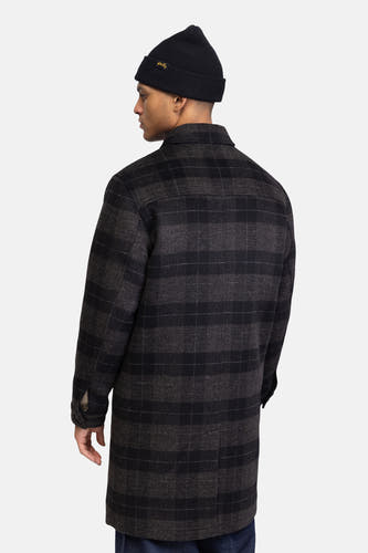 Manteau long noir de REDEFINED REBEL, avec un motif à carreaux et porté avec une beanie noire.