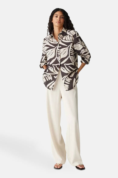 Chemise brune à longues manches d'OPUS, avec un motif abstrait de feuilles et portée avec un pantalon blanc.