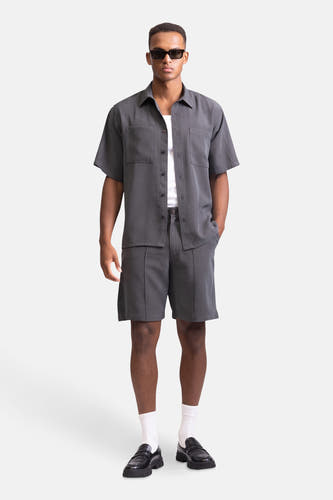 Short gris de REDEFINED REBEL, associé à un chemisier gris, des chaussettes blanches et des loafers noirs.