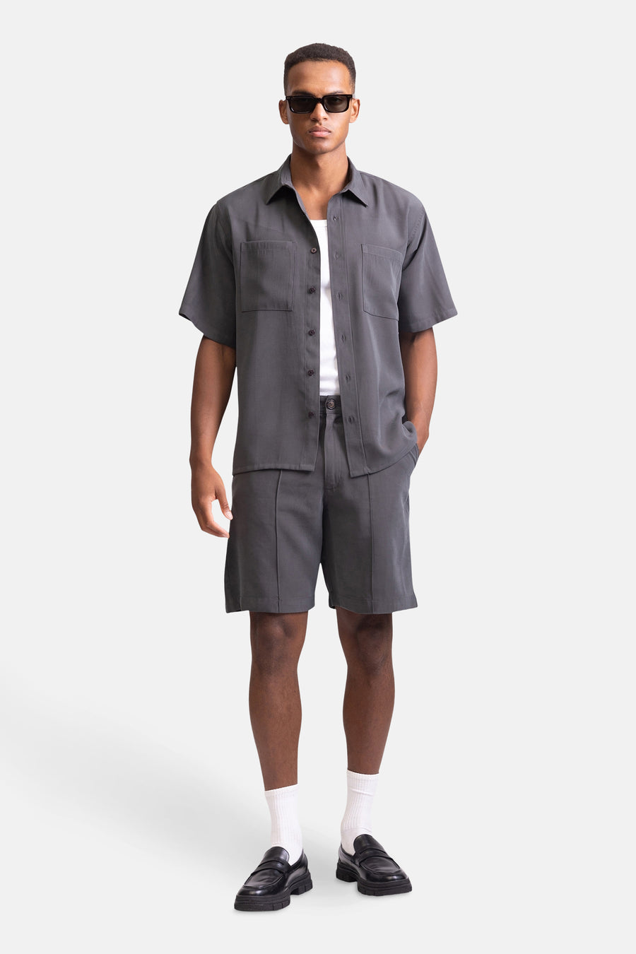 Short gris de REDEFINED REBEL, associé à un chemisier gris, des chaussettes blanches et des loafers noirs.