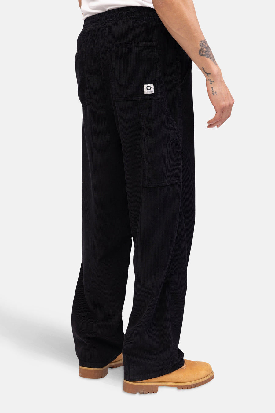 Pantalon noir de REDEFINED REBEL, texture corduroy, avec poches, vu en profil, associé à des chaussures brunes.