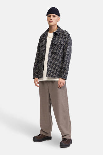 Pantalon brun de REDEFINED REBEL, associé à une veste imprimée, un t-shirt blanc, une chaîne dorée et des chaussures noires.