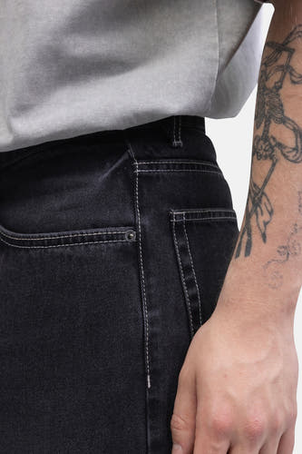Jeans coupe large en denim gris foncé de REDEFINED REBEL, avec surpiqûres blanches et un bras tatoué.