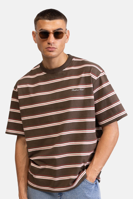 T-shirt multicolore de REDEFINED REBEL, avec des rayures horizontales marron, blanc et rouge, porté par un homme avec des lunettes de soleil.
