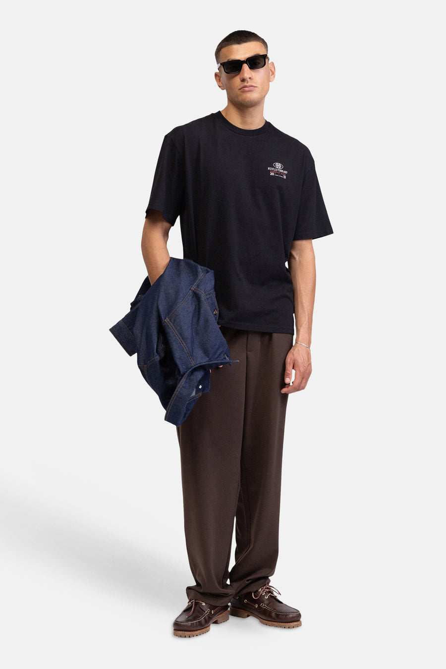 T-shirt noir de REDEFINED REBEL avec imprimé poitrine blanc et rouge, porté par un homme avec une veste en jean et un pantalon marron.