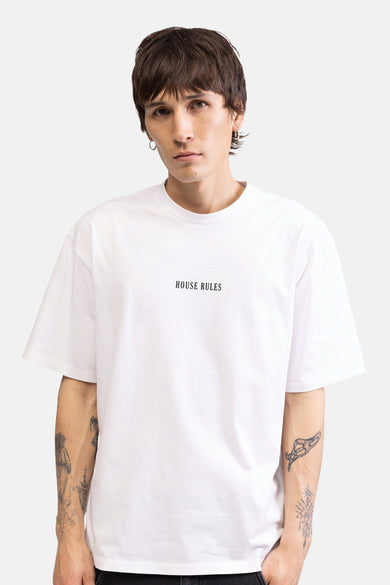 T-shirt blanc REDEFINED REBEL avec un grand imprimé graphique 'Society House Rules' dans le dos, porté par un homme tatoué.