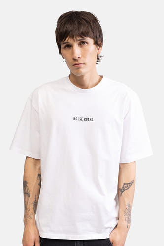 T-shirt oversize blanc de REDEFINED REBEL avec le texte 'HOUSE RULES' sur la poitrine, porté par un mannequin tatoué.