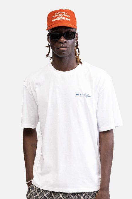 T-shirt blanc REDEFINED REBEL avec imprimé palmier et textes dans le dos, porté par une personne avec une casquette orange.