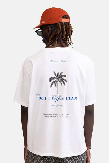 Wit T-shirt van REDEFINED REBEL met palmboomprint en teksten op de rug, gedragen door een persoon met oranje pet.