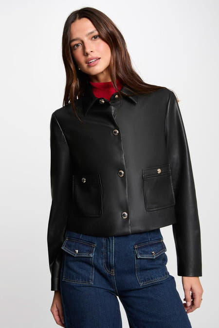 Manteau court noir de Morgan De Toi avec fermeture à boutons, poches et associé à un gilet rouge et des jeans.