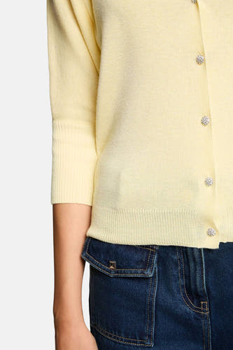 Cardigan Morgan De Toi en maille fine de couleur jaune avec manches trois-quarts, bords-côtes aux manches et à la base, et boutons scintillants, partiellement sur un jean bleu foncé.