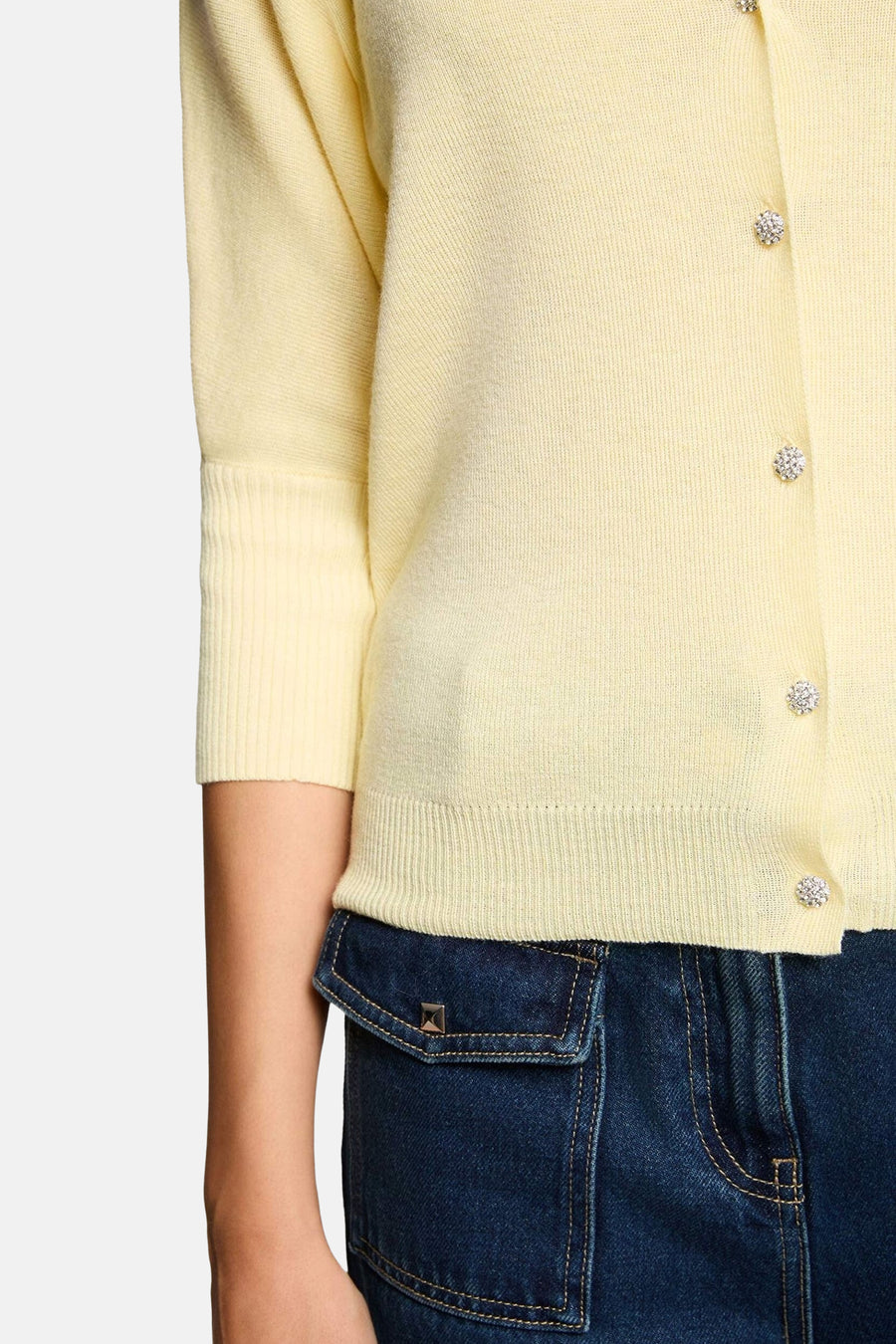 Cardigan Morgan De Toi en maille fine de couleur jaune avec manches trois-quarts, bords-côtes aux manches et à la base, et boutons scintillants, partiellement sur un jean bleu foncé.