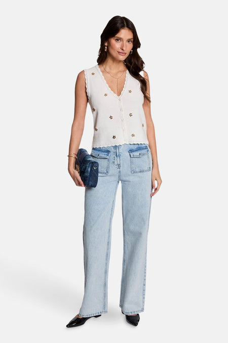 Gilet blanc de Morgan De Toi, avec motif floral, porté avec des jeans larges et des chaussures noires.