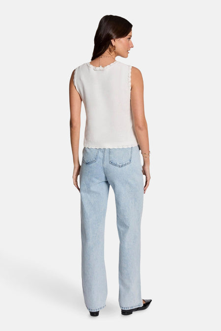 Gilet blanc de Morgan De Toi, avec des bords décoratifs, associé à des jeans bleu clair et des chaussures noires.