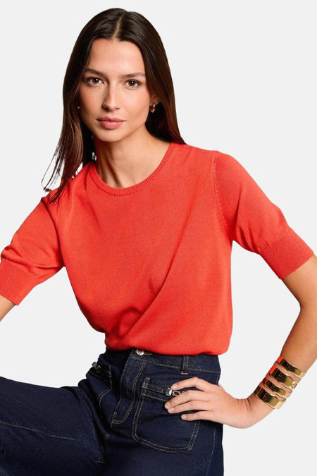 Maillot orange avec col rond de Morgan De Toi, porté avec un jeans foncé et des bracelets en or.