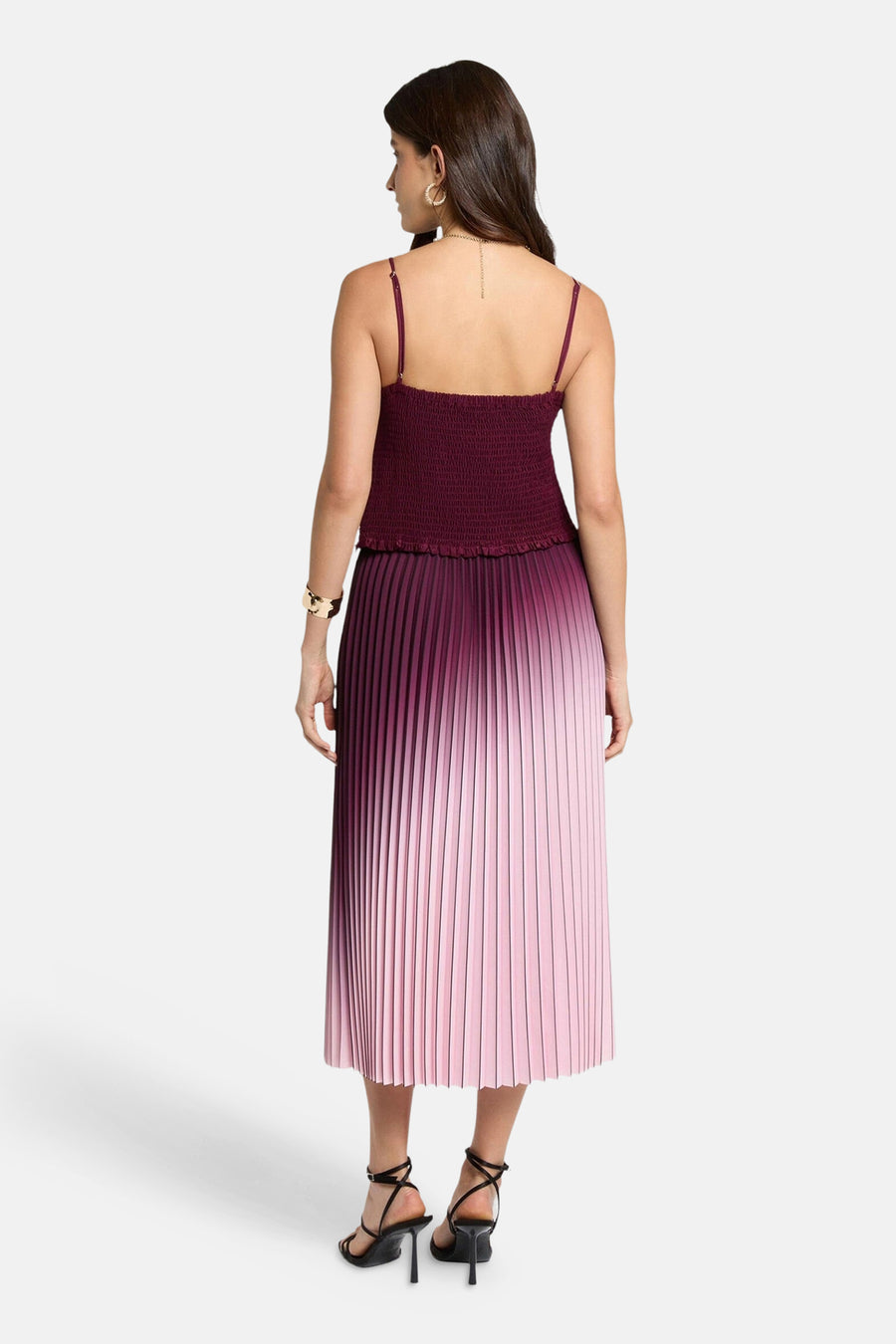 Bordeaux mouwloze top van Morgan De Toi, met een geplisseerde rok met ombre-effect, gedragen met een gouden armband en zwarte hakken.
