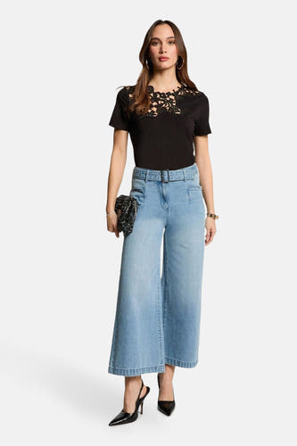 Jean en denim bleu clair large de Morgan De Toi, avec ceinture, associé à une chemise noire et des baskets noires.