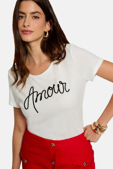 T-shirt blanc de Morgan De Toi avec une lettre 'Amour' noire, associé à un pantalon rouge et des bracelets d'or.